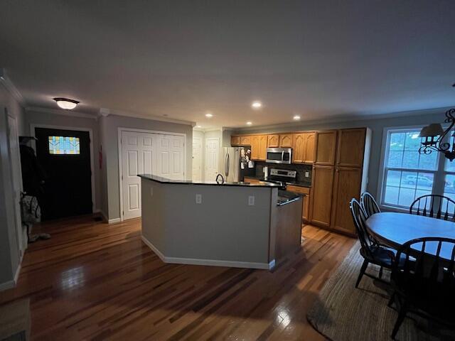 kitchen with dark hardwood / wood-style floors, a chandelier, a kitchen island with sink, appliances with stainless steel finishes, and ornamental molding