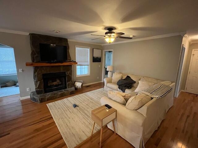 living room featuring hardwood / wood-style floors, a stone fireplace, ceiling fan, and crown molding