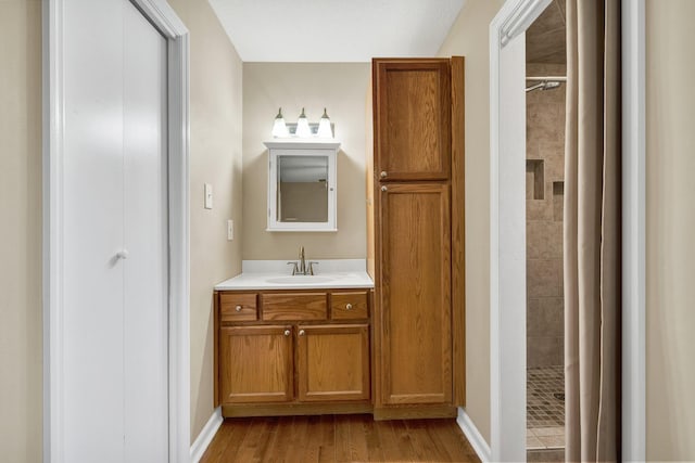 bathroom featuring vanity, baseboards, wood finished floors, and tiled shower