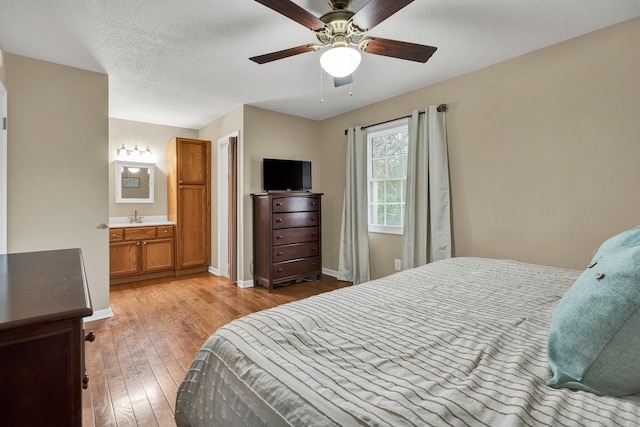 bedroom featuring light wood-type flooring, baseboards, a textured ceiling, a sink, and ensuite bath