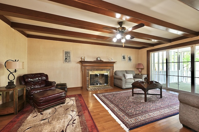 living room featuring ceiling fan, wood finished floors, beam ceiling, and a fireplace