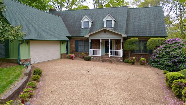 new england style home with concrete driveway, covered porch, an attached garage, brick siding, and roof with shingles