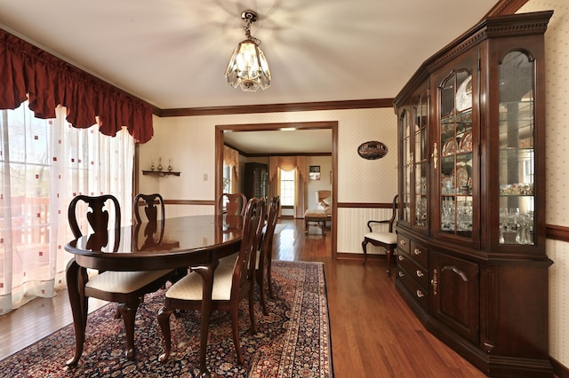 dining room with a notable chandelier, wallpapered walls, wainscoting, dark wood finished floors, and ornamental molding