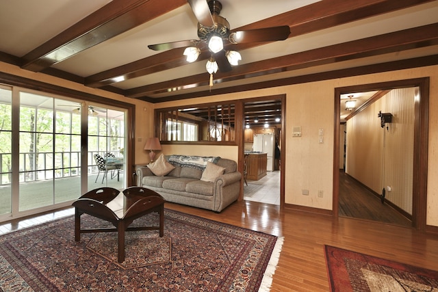 living area with baseboards, a ceiling fan, wood finished floors, and beamed ceiling