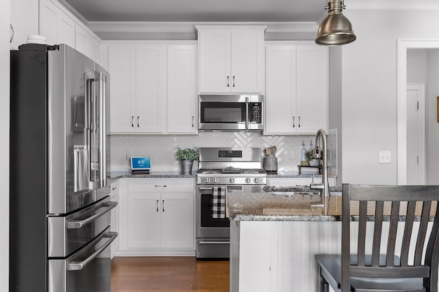 kitchen with sink, dark stone countertops, stainless steel appliances, white cabinets, and decorative light fixtures