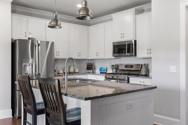 kitchen featuring sink, hanging light fixtures, stainless steel appliances, white cabinets, and a center island with sink