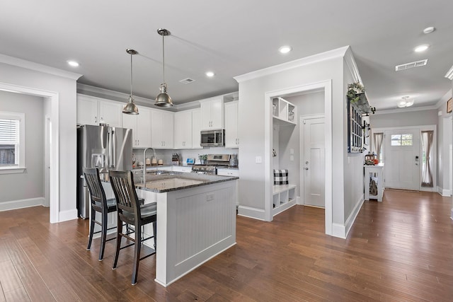 kitchen with appliances with stainless steel finishes, white cabinetry, sink, dark stone countertops, and a kitchen bar