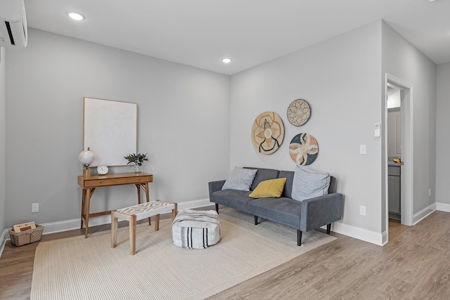 living room with a wall unit AC and light hardwood / wood-style flooring