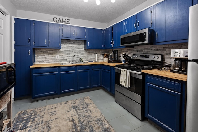 kitchen with light tile patterned floors, blue cabinetry, a sink, stainless steel appliances, and butcher block counters