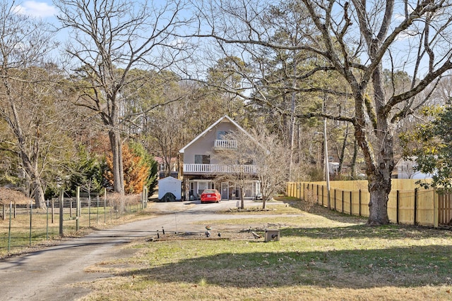 view of front facade with a balcony, fence, a front lawn, and dirt driveway