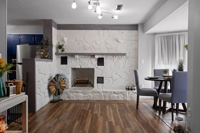 living room featuring a stone fireplace, wood finished floors, visible vents, and a textured ceiling