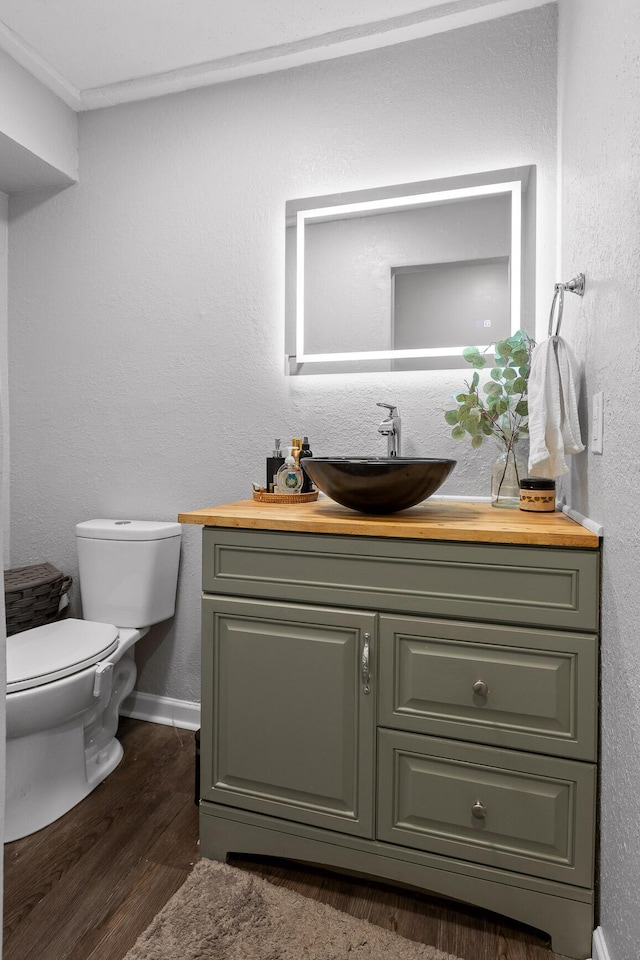 bathroom with toilet, wood finished floors, vanity, and a textured wall