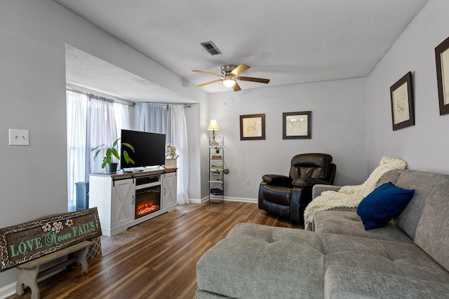 living room featuring dark wood-style floors, visible vents, a textured ceiling, and ceiling fan