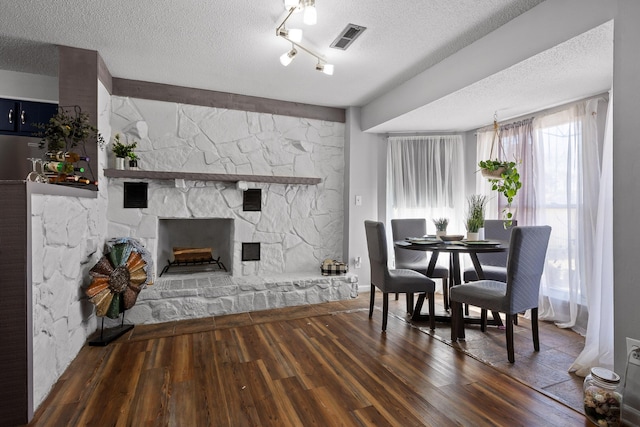 dining space featuring a fireplace, wood finished floors, visible vents, and a textured ceiling