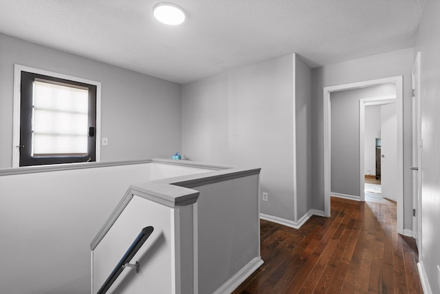 hallway with an upstairs landing, dark wood-style floors, a textured ceiling, and baseboards