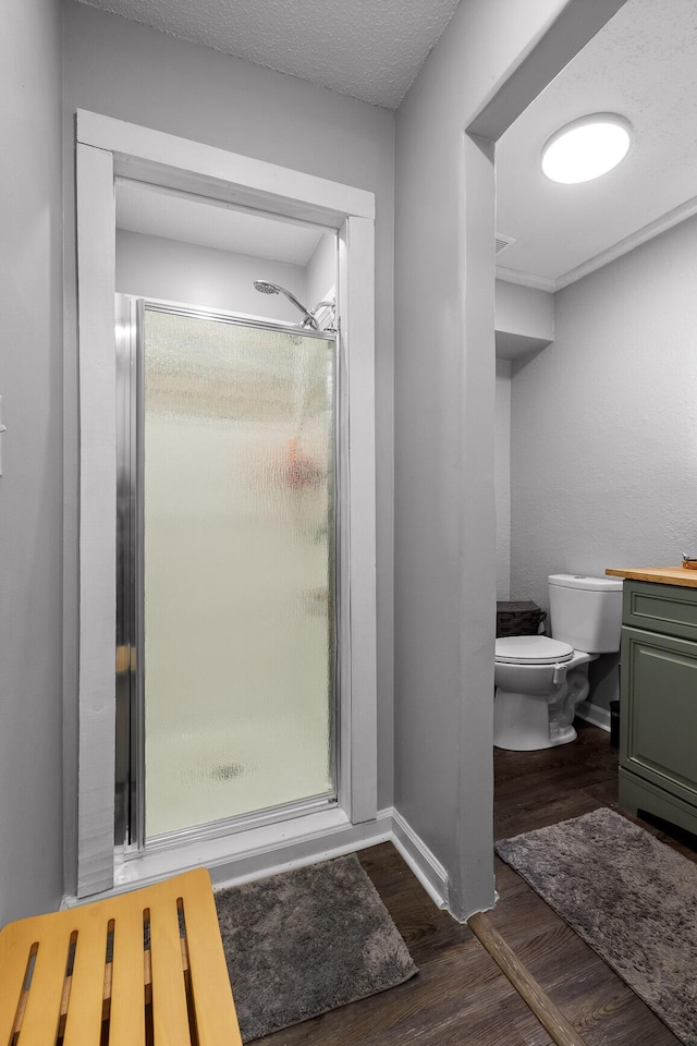 bathroom with a shower stall, baseboards, toilet, wood finished floors, and a textured ceiling