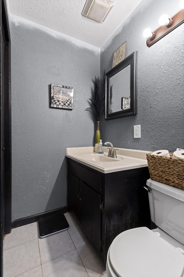 half bathroom with vanity, visible vents, tile patterned flooring, toilet, and a textured wall