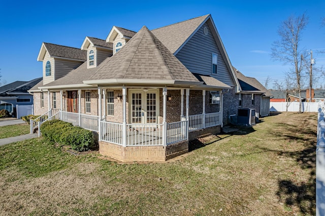 view of front of property featuring a shingled roof, covered porch, cooling unit, a front lawn, and brick siding