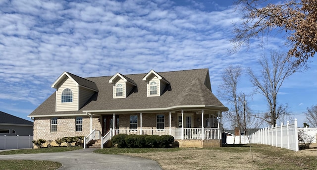 view of front of home with a porch, brick siding, fence, roof with shingles, and a front yard