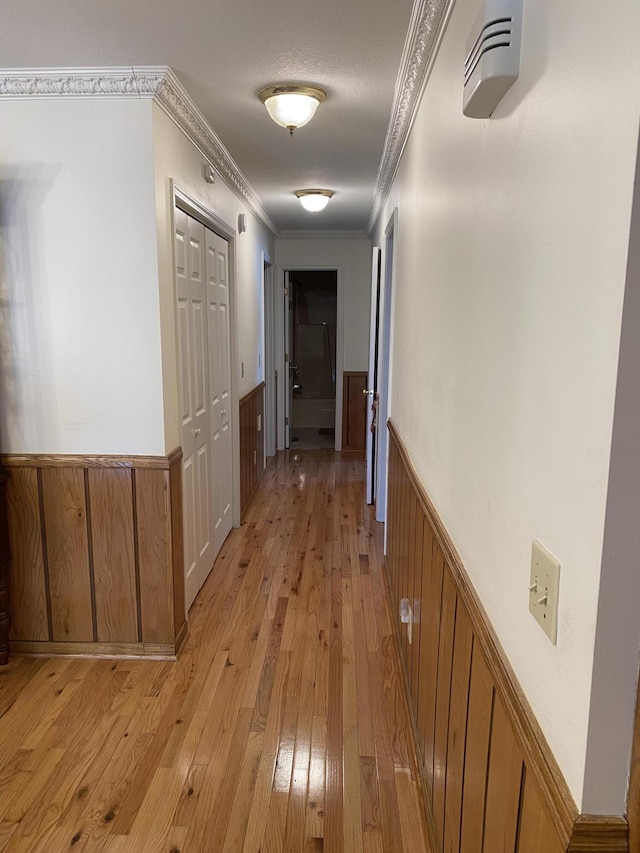 hall with light wood-type flooring, a wainscoted wall, and crown molding