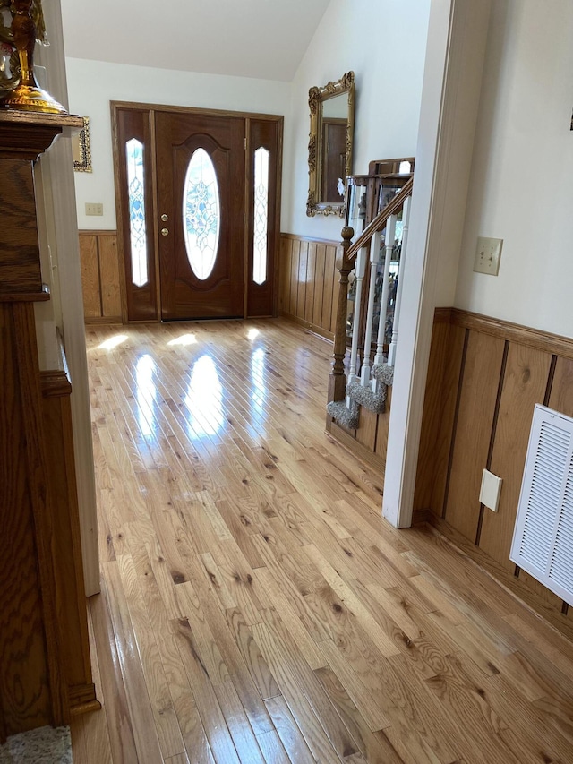 entryway featuring a wainscoted wall, lofted ceiling, visible vents, light wood-style floors, and stairs