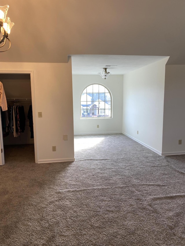 carpeted spare room with an inviting chandelier and baseboards