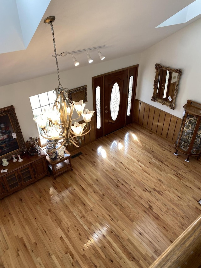 foyer with a wainscoted wall, an inviting chandelier, lofted ceiling with skylight, track lighting, and wood finished floors