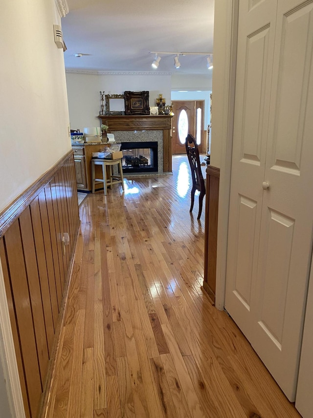 corridor featuring rail lighting, a wainscoted wall, and light wood finished floors