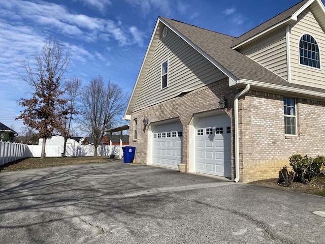 view of side of property featuring a shingled roof, fence, brick siding, and aphalt driveway