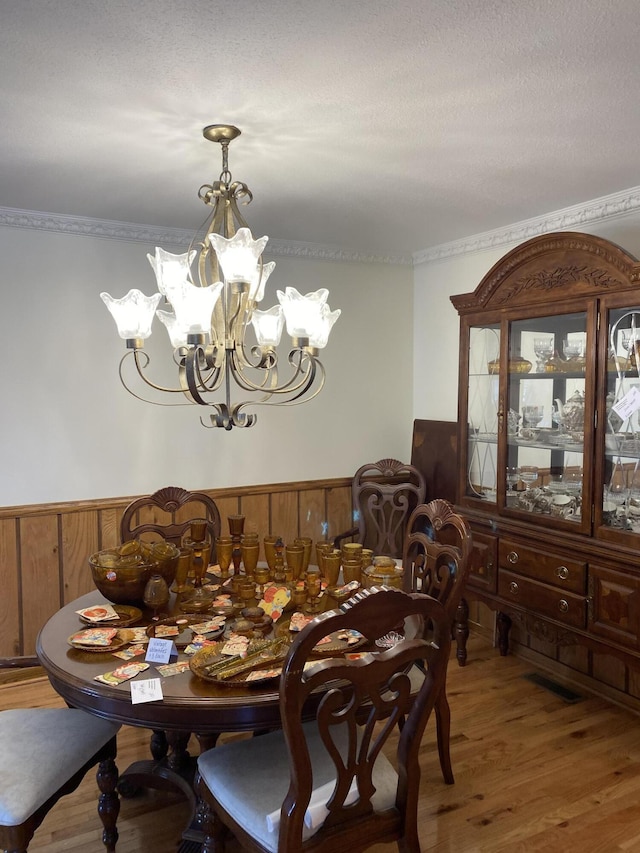 dining area featuring a wainscoted wall, ornamental molding, wood finished floors, and an inviting chandelier