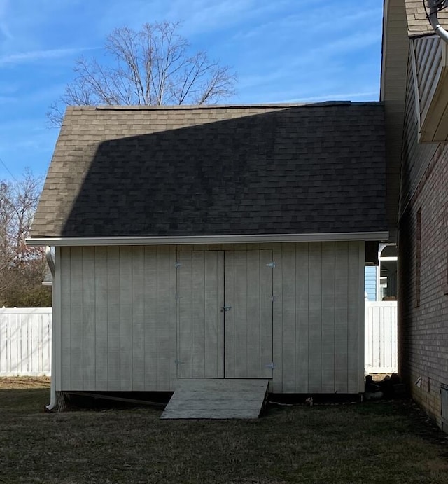 view of property exterior featuring a shingled roof, fence, an outdoor structure, and a storage unit