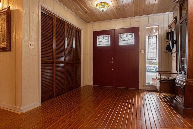 foyer featuring wood walls, wood-type flooring, wooden ceiling, and ornamental molding