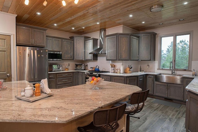 kitchen with sink, stainless steel appliances, wall chimney range hood, light stone counters, and a breakfast bar area