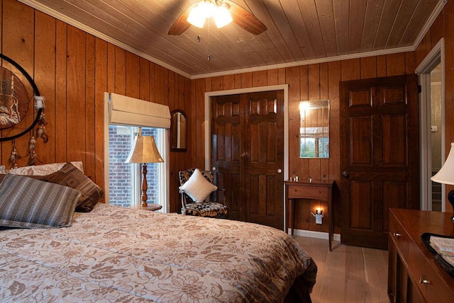 bedroom featuring ceiling fan, wooden ceiling, wood walls, crown molding, and a closet