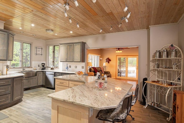 kitchen featuring track lighting, light stone counters, a kitchen island, and sink