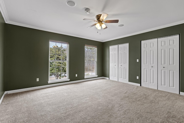 unfurnished bedroom featuring multiple closets, ceiling fan, ornamental molding, and carpet flooring