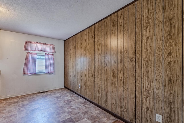 unfurnished room with wood walls, a textured ceiling, and tile patterned floors