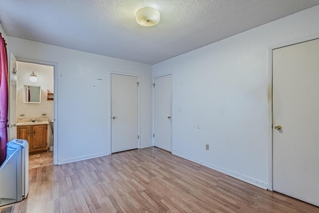 unfurnished bedroom with a textured ceiling, light wood finished floors, baseboards, and ensuite bathroom