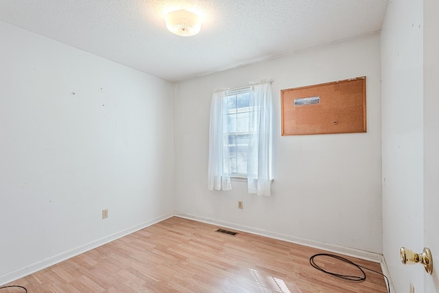 spare room featuring light wood-type flooring, baseboards, visible vents, and a textured ceiling