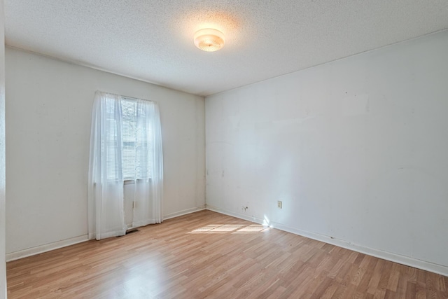 empty room with light wood-style floors, baseboards, and a textured ceiling