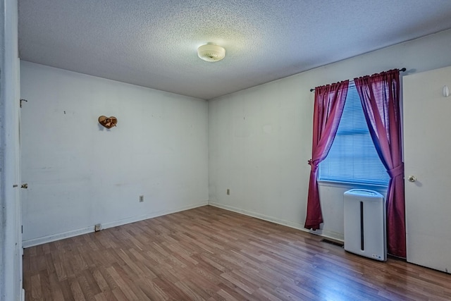 spare room featuring a textured ceiling, baseboards, and wood finished floors