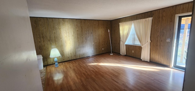 empty room featuring wooden walls, a textured ceiling, and wood finished floors