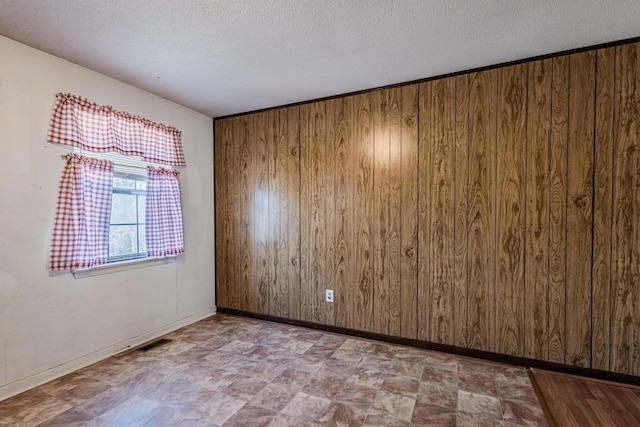 spare room with baseboards, visible vents, wooden walls, and a textured ceiling