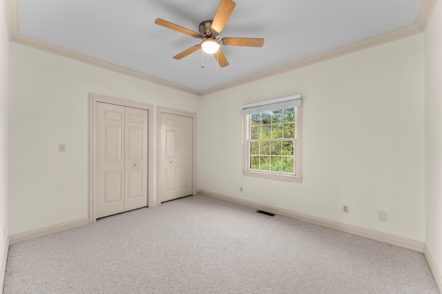 unfurnished bedroom with multiple closets, carpet floors, visible vents, baseboards, and ornamental molding
