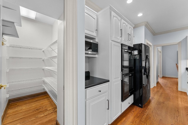 kitchen featuring dark countertops, light wood-type flooring, white cabinetry, black appliances, and ornamental molding