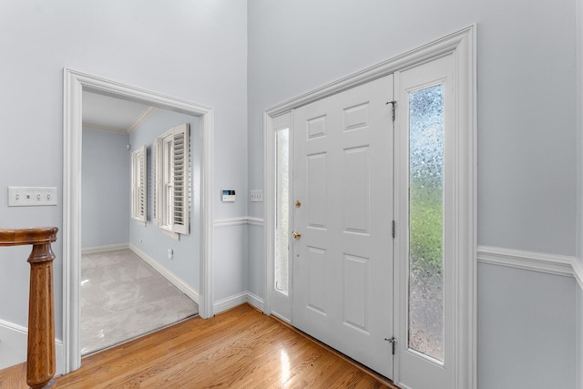 entryway with baseboards, crown molding, light wood-type flooring, and light colored carpet