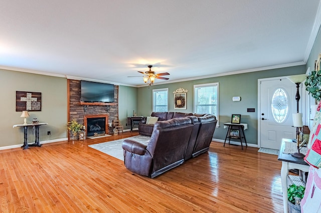 living room with ceiling fan, hardwood / wood-style flooring, crown molding, and a stone fireplace