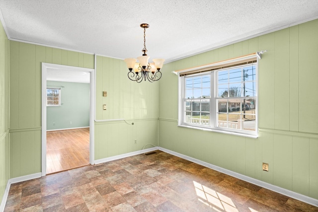 unfurnished dining area featuring ornamental molding, a textured ceiling, and a chandelier