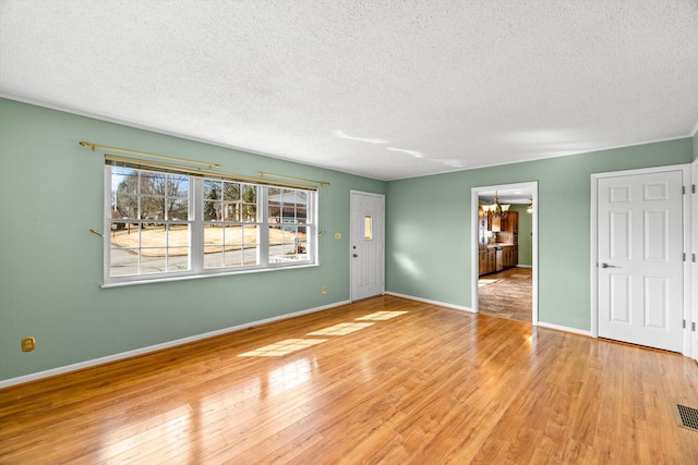 empty room featuring light hardwood / wood-style flooring, a chandelier, and a textured ceiling