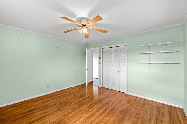 unfurnished bedroom featuring wood-type flooring, a textured ceiling, ornamental molding, a closet, and ceiling fan